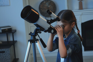 Cute little girl looking at stars through telescope in room