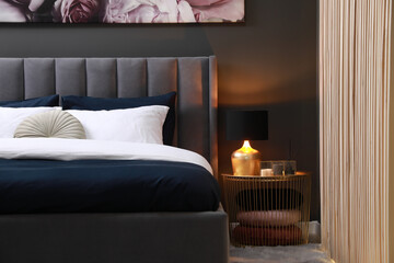 Comfortable bed with cushions, lamp and different decor on bedside table in room. Stylish interior