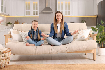 Mother with daughter meditating on sofa at home. Harmony and zen - obrazy, fototapety, plakaty