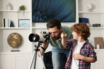 Little boy with his father looking at stars through telescope in room
