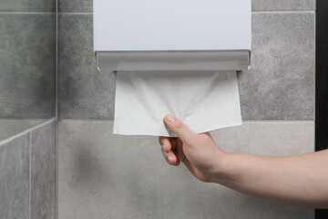 Woman taking new fresh paper towel from dispenser in bathroom, closeup
