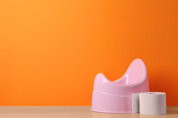 Pink baby potty and toilet paper on wooden table against orange background, space for text