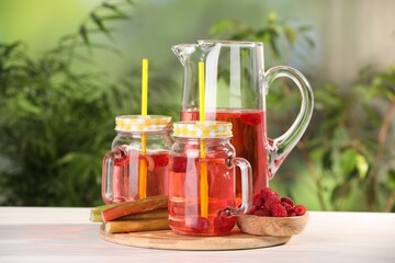 Tasty rhubarb cocktail with raspberry and stalks on white wooden table outdoors