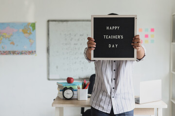 A man showing lettering board with text Happy Teacher's Day  to the camera and standing inside...