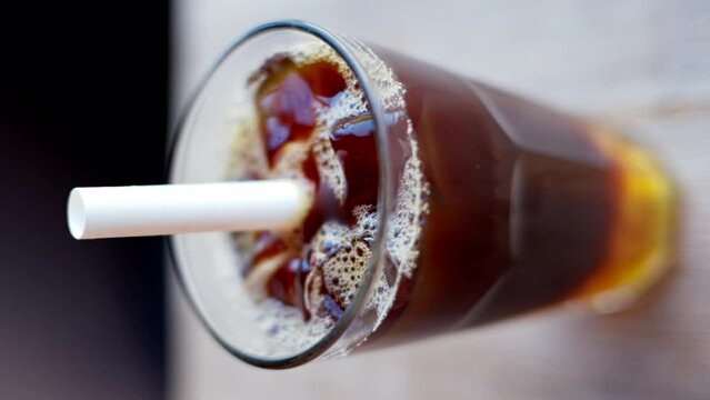 Cold brew coffee and bubble tea in a glass with ice and big white straw close up slow motion, vertical screen