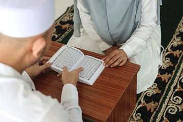 Over shoulder view of Asian muslim man teaching his wife reading Koran or Quran in mosque. Muslim...