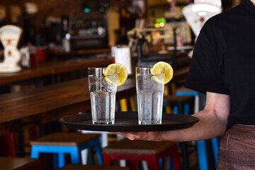 Restaurant server holding a tray with two glasses with water and lemon slice
