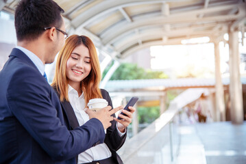 Businessman Businesswoman drinking coffee in town using smartphone outside office modern city. Hands holding take away coffee cup and smart phone talking together Business partner with cup of coffee