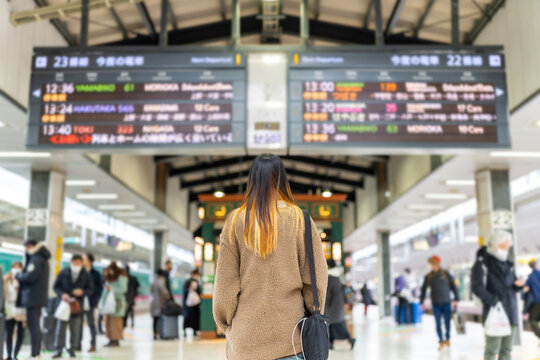 Young Asian woman looking at timetable schedule during waiting for the train at railway station. Attractive girl enjoy outdoor lifestyle travel city by railroad transportation on holiday vacation.