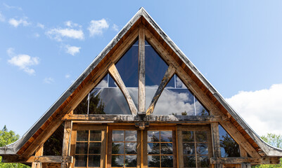 vue sur le haut d'une maison en bois avec la façade en verre lors d'une journée ensoleillée avec la réflection du ciel dans la vitre