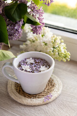 Tasty black tea in white cup on windowsill with aromatic lilac flowers. Spring composition Cup of lilac tea drinking recipe flowering branches of purple lilac. Still life for copy space greeting card