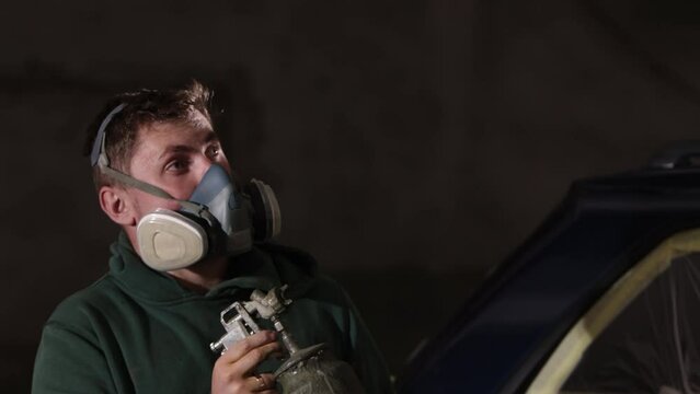 Safety measures, Safety procedures, Safety guidelines. Man straps on gas mask in preparation for car painting task.