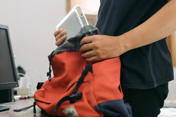 A young man packing book into a bag on the table inside room