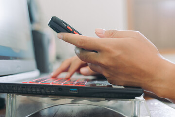 Hands of Asian man holding checking smartphone while typing on laptop keyboard