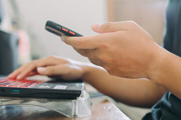 Hands of Asian man holding checking smartphone while typing on laptop keyboard