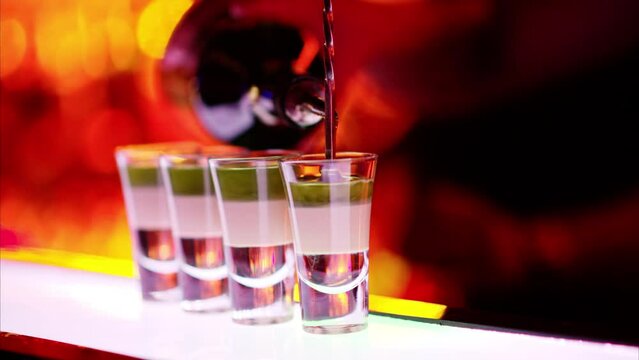 Barman making cocktail shots with liquor alcohol in three layers at the bar at night with red neon lights, slow motion