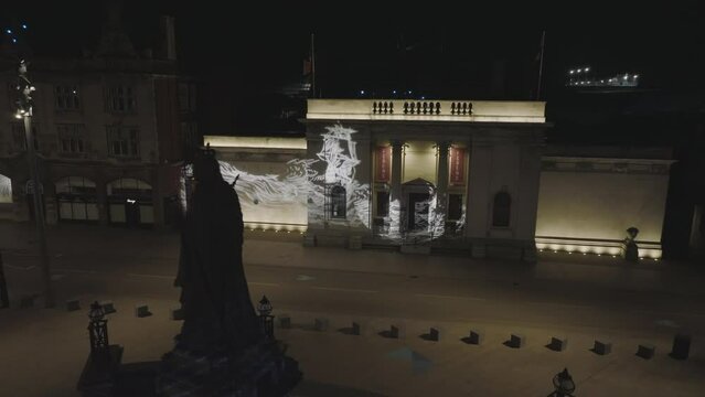 Slow panning by the statue of Queen Victoria located in Hull's Queen Victoria Square, continuing into a fly around of the Scrimshaw Gobos projected onto Ferens Art Gallery. 