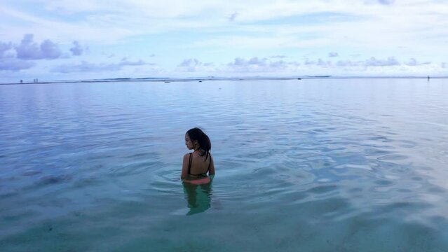 A Woman Traveler Swims On Crystal Clear Beach Of Gunung Payung In Bali, Indonesia. Aerial Drone Shot