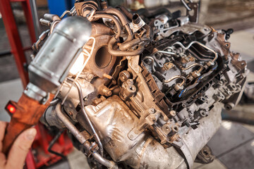 A car mechanic inspects the engine with a flashlight. Engine Block on a repair stand with Special crane jack. Technical service station for car.