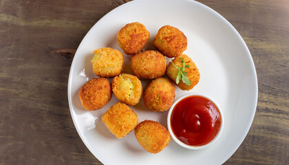 delicious potato croquettes - mashed potatoes balls with grated mozzarella cheese seasoned with spices; breaded and deep fried in olive oil, served with ketchup on white plate, view from above