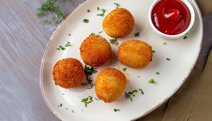 delicious potato croquettes - mashed potatoes balls with grated mozzarella cheese seasoned with spices; breaded and deep fried in olive oil, served with ketchup on white plate, view from above