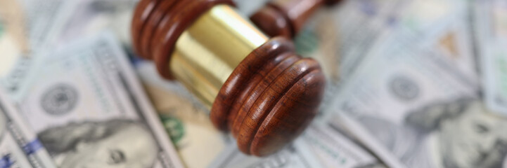 Wooden judge gavel on dollar bills background, shallow focus.