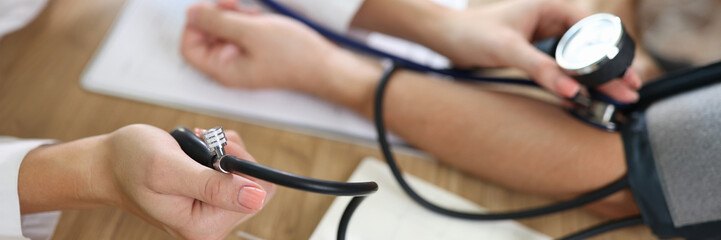 Close up of doctor using sphygmomanometer with stethoscope checks blood pressure of patient in...