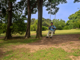 Senior man playing on a swing in the forest of Nokojima, Fukuoka City, Fukuoka Prefecture, Japan