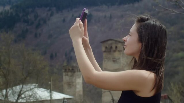 Young woman taking pictures of old stone towers in the mountains. View of traditional ancient Georgian architecture in Svaneti. Cultural heritage