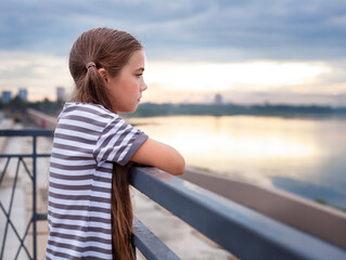 Cute little girl in striped t-shirt standing on the bridge and looking away