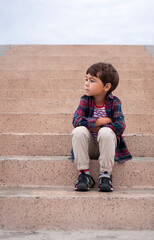 Cute little boy sitting on the stairs. Outdoors portrait.