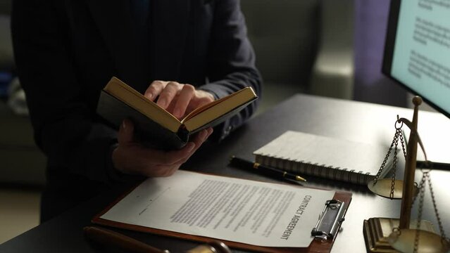 Asian male lawyer or legal advisor working on the scale of justice sitting at her desk and holding a pen to look at the information Detailed content about the scale of jurisprudence to study.