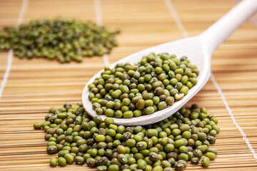 A wooden spoon filled with mung beans on top of a bamboo mat