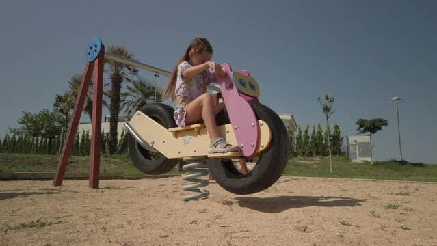 Young girl having fun playing on a playground spring rocker motorbike
