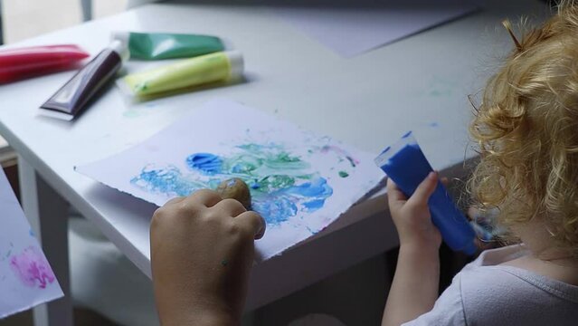 Toddler painting with potatoes and blue ink on her table.