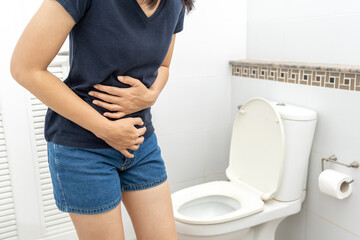 Female suffers from diarrhea hand holding stomach in front toilet bowl. Woman squeezing tissue with...