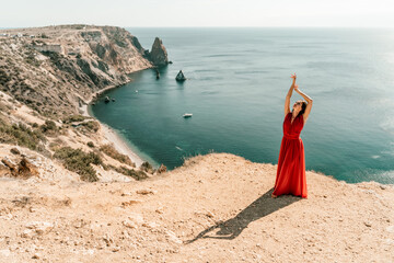 Woman red dress sea. posing on a rocky outcrop high above the sea. Girl on the nature on blue sky background. Fashion photo.