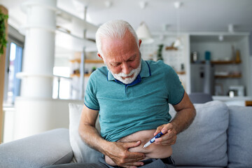 Senior man using lancet pen at home. Diabetes control Mature man sitting and injecting insulin