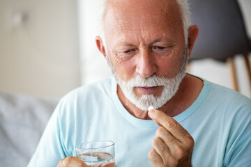 Senior man takes pill with glass of water in hand. Stressed mature man drinking sedated antidepressant meds. Man feels depressed, taking drugs. Medicines at work