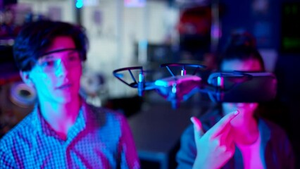 Young engineers with VR virtual reality headset controlling fliying drone in research laboratory, slow motion, neon blue pink lights - Powered by Adobe