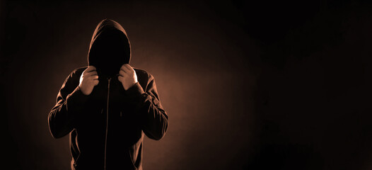 Anonymous man in hood on black background, space for text. Banner design, color toned