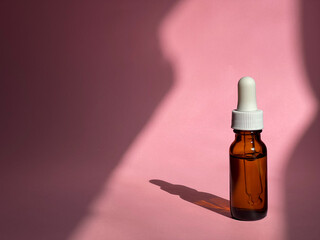 Cosmetic transparent jar with serum on a pink background with sunlight on it. Beauty routine