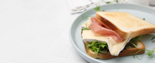 Tasty sandwich with brie cheese and prosciutto on white table, closeup. Banner design with space for text