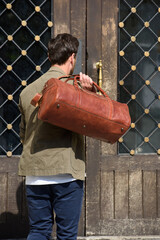 a man with a bag. black leather travel bag, street photo. man is wearing blue sneakers, jeans, a white T-shirt and a jacket