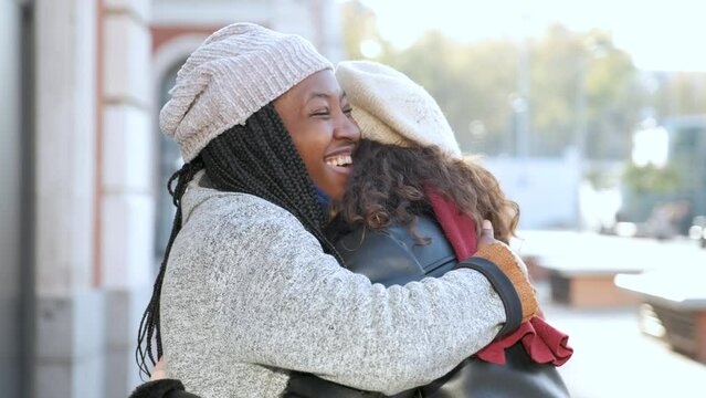 Two Multiracial Female Happy Friends Hugging Each Other And Smiling On City Street.