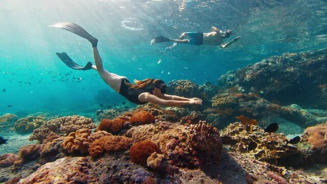 Couple freediving. Young fit freedivers man and woman swim underwater over the healthy coral reef near the island of Nusa Penida in Bali, Indonesia