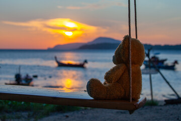 .lonely Teddy Bear sitting on a swing in front Rawai beach to see sunrise..scenic reflection of...