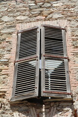 window in a stone wall with old weathered wooden shutters almost closed to shut out the hot summer sun
