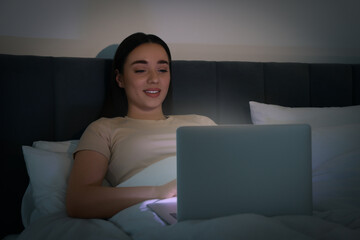 Young woman using laptop in bed at night. Internet addiction