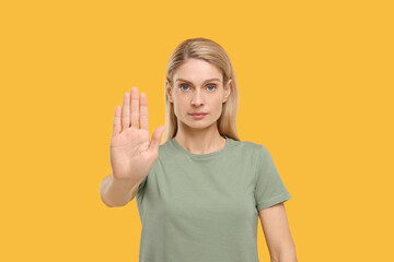 Woman showing stop gesture on yellow background